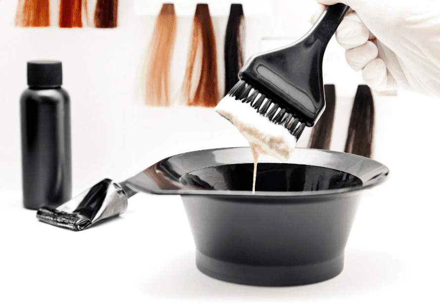 Hair dye brush and bowl with color samples in the background.